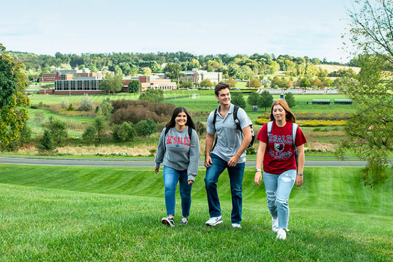 A group of students walking in a field with a campus in  the background